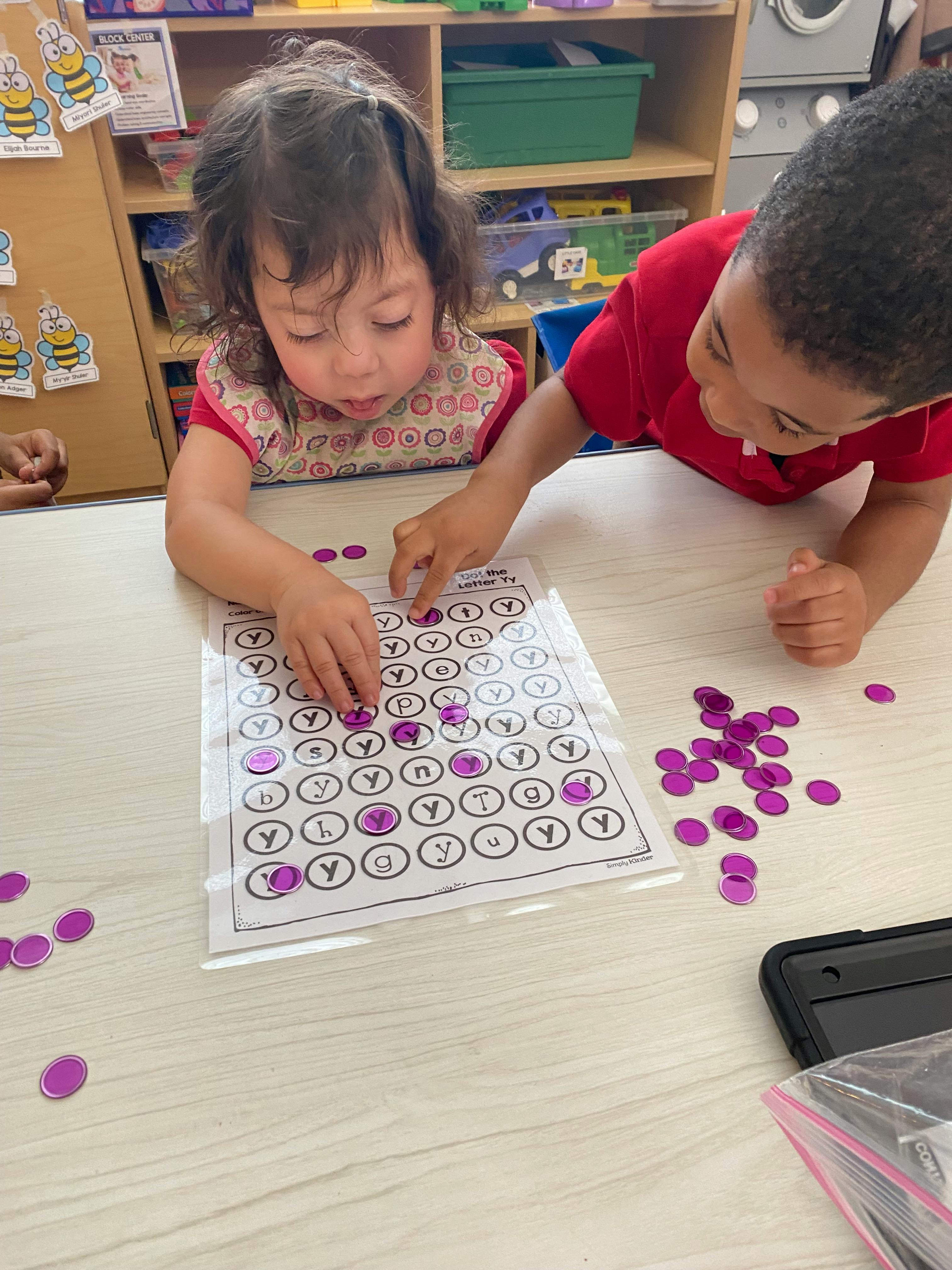 Two children at a table, placing purple chips on a worksheet with the letter Y