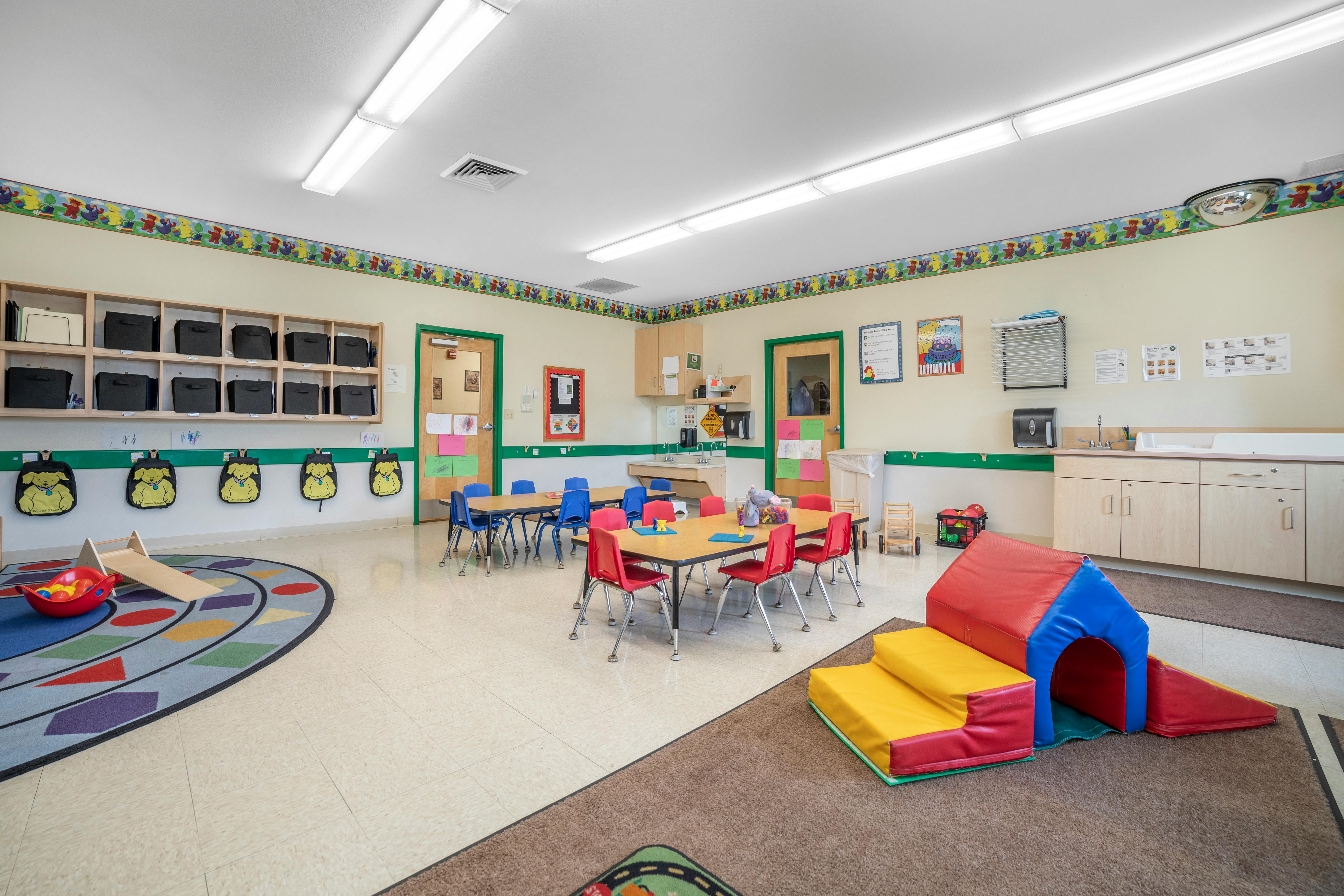 Classroom with small tables and chairs, play mats, and cubbies