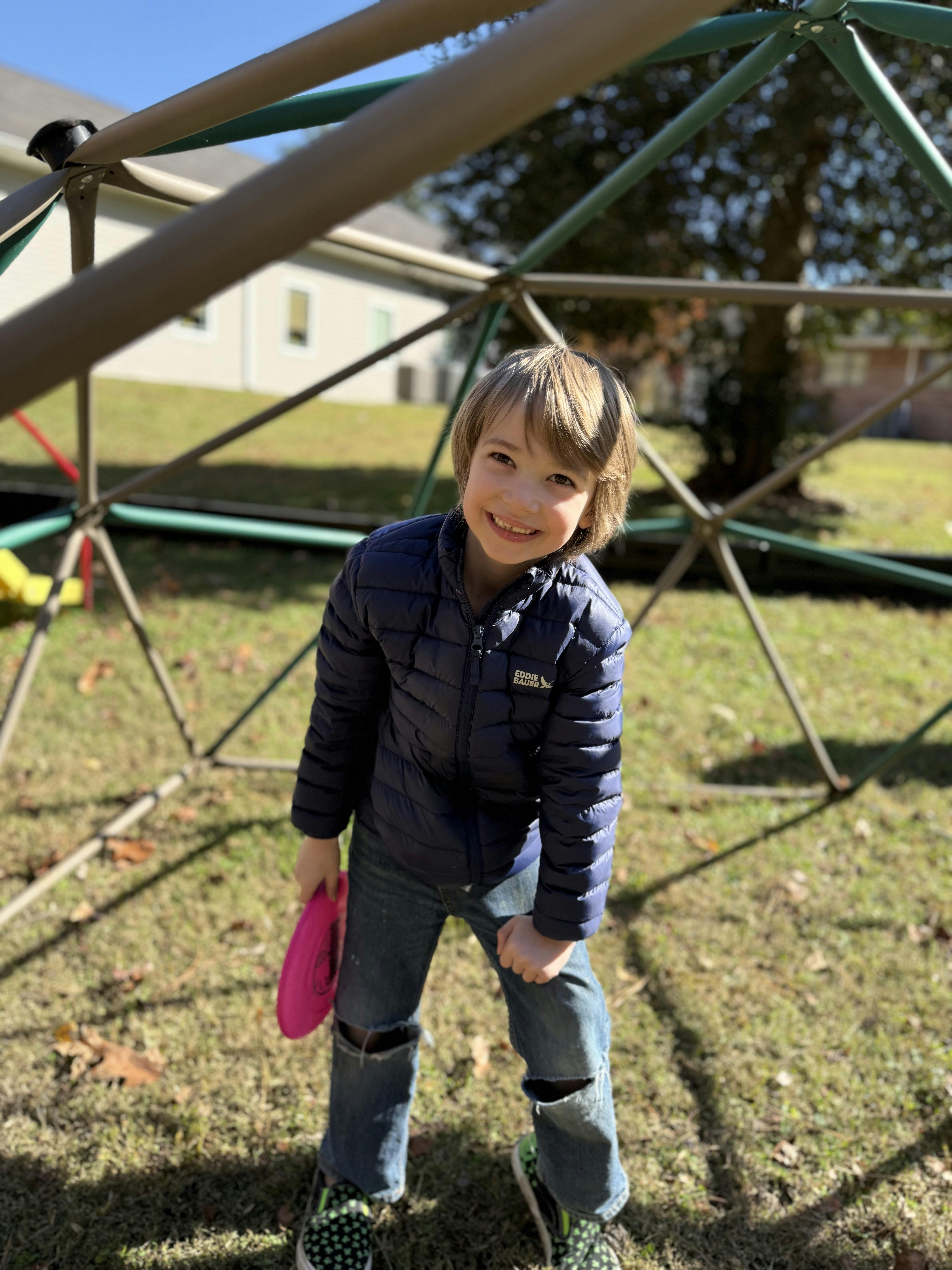 Child smiling while holding a pink frisbee on a geometric dome climber
