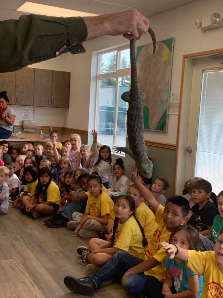 Person holding a lizard by its tail in front of seated children
