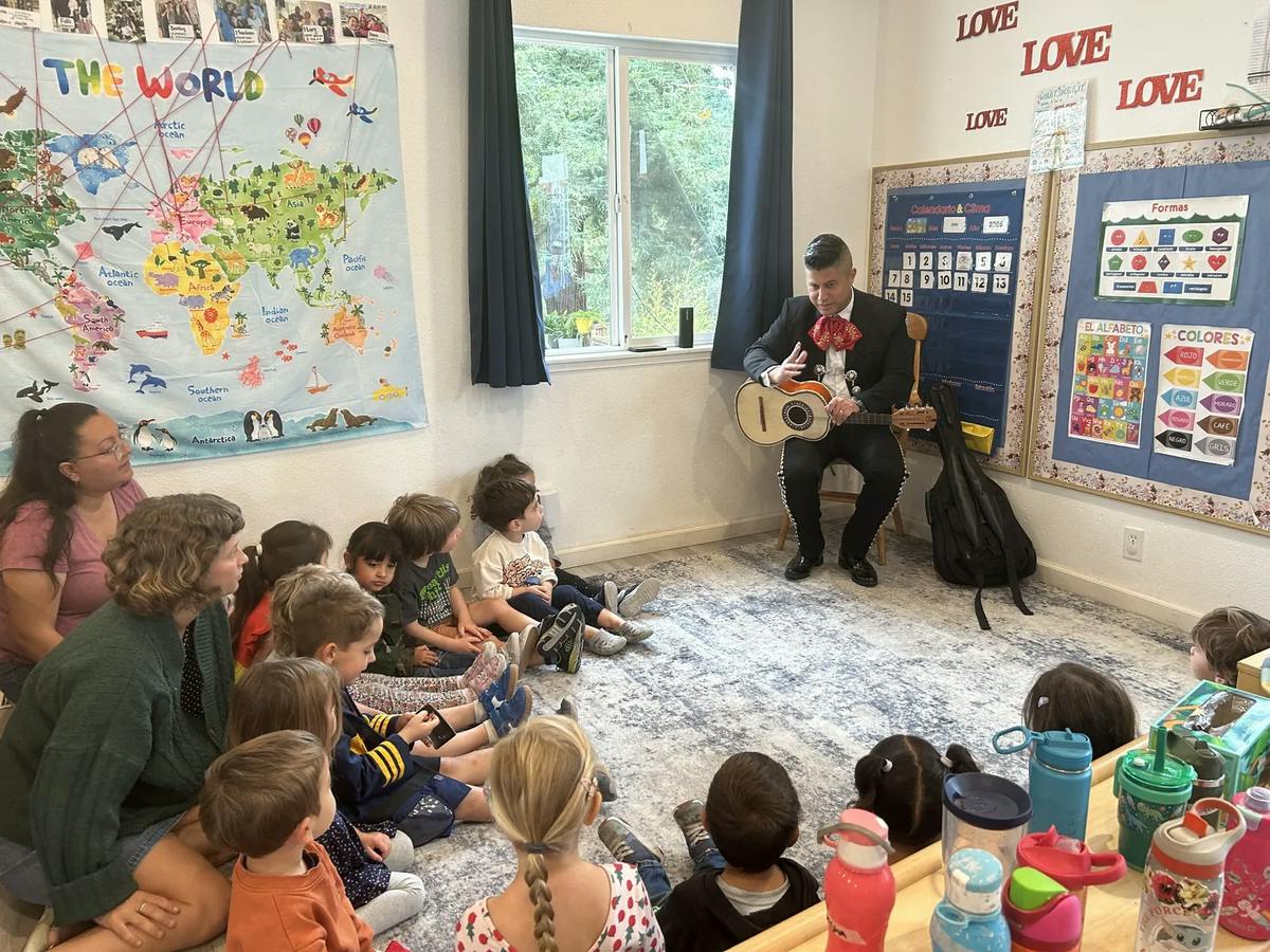 Person in mariachi attire playing guitar for a group of children in a classroom