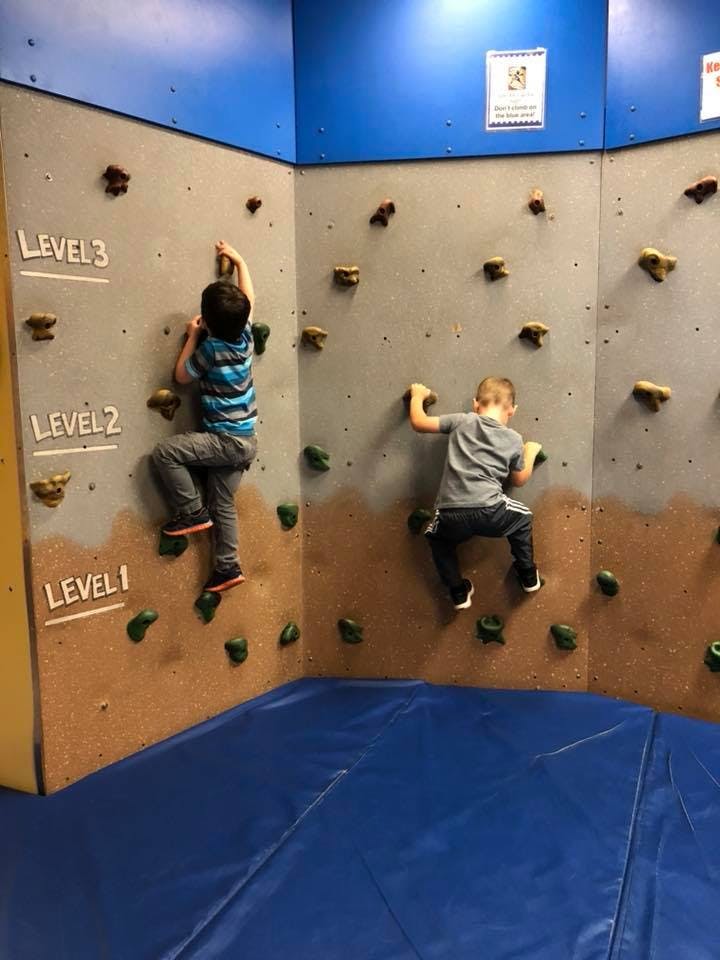 Two children climbing on an indoor rock wall with level markers