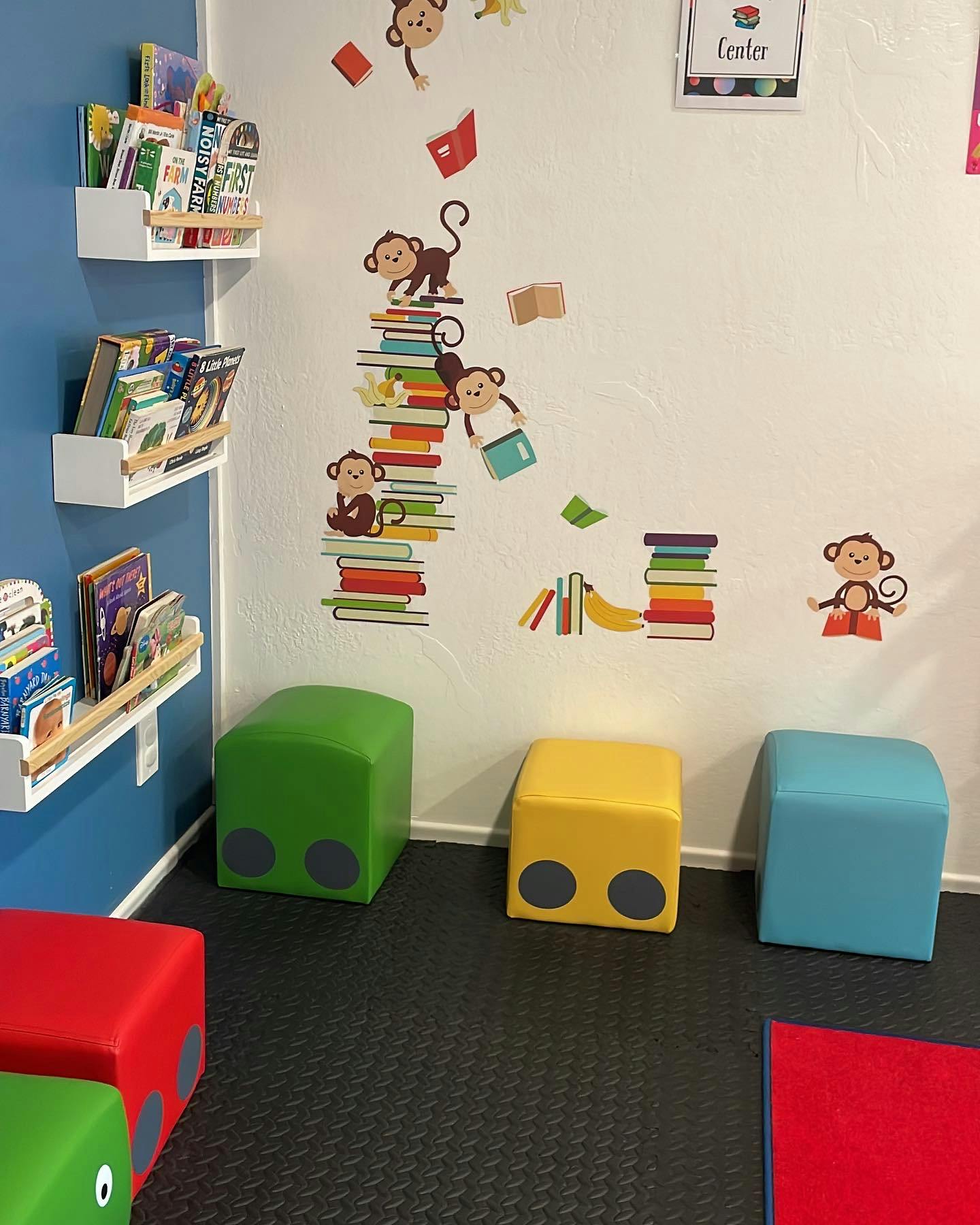 Children's reading nook with colorful floor cushions and monkey wall decals