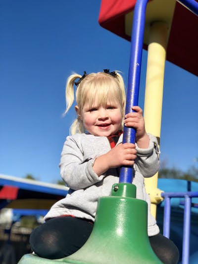 Child with pigtails holding onto a blue pole on a playground