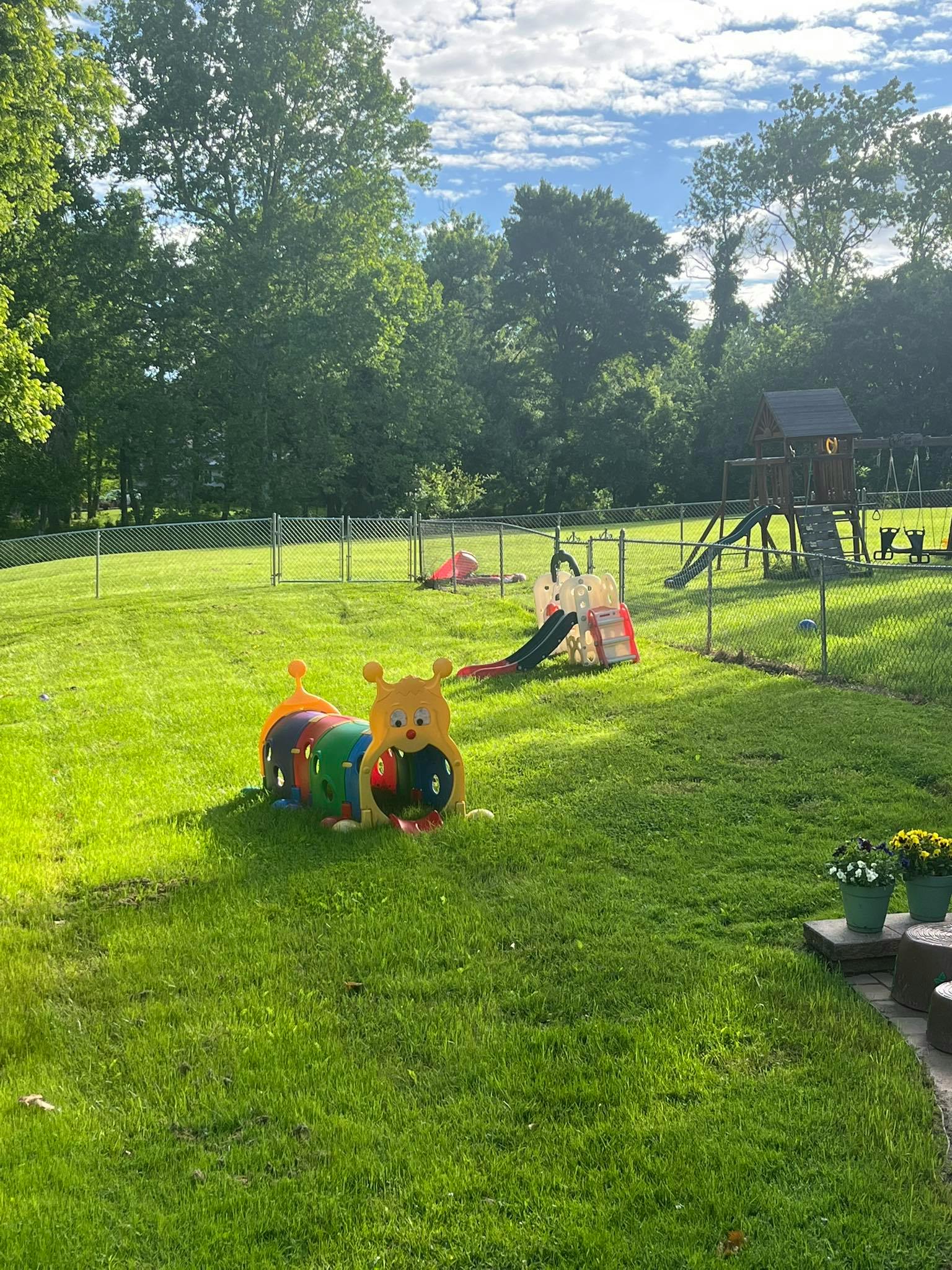 Playground with a caterpillar tunnel, slide, and swing set in a grassy yard