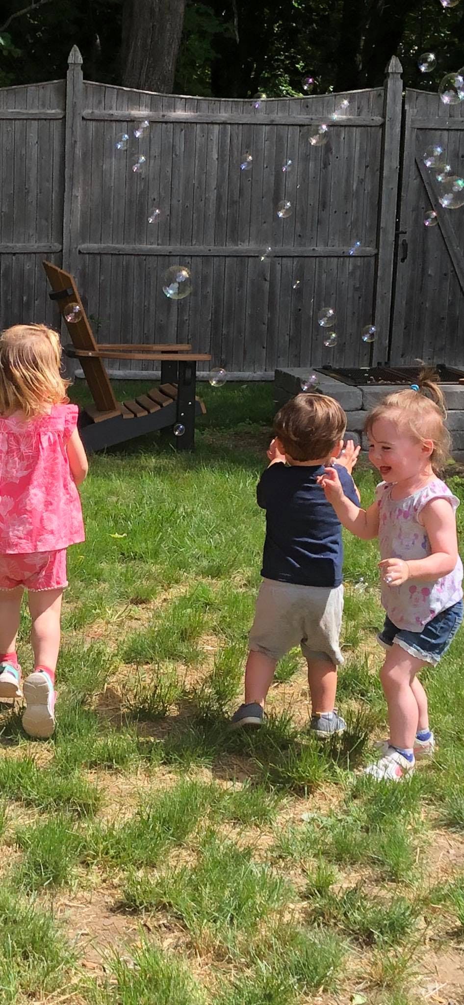 Three children playing with bubbles in a grassy yard