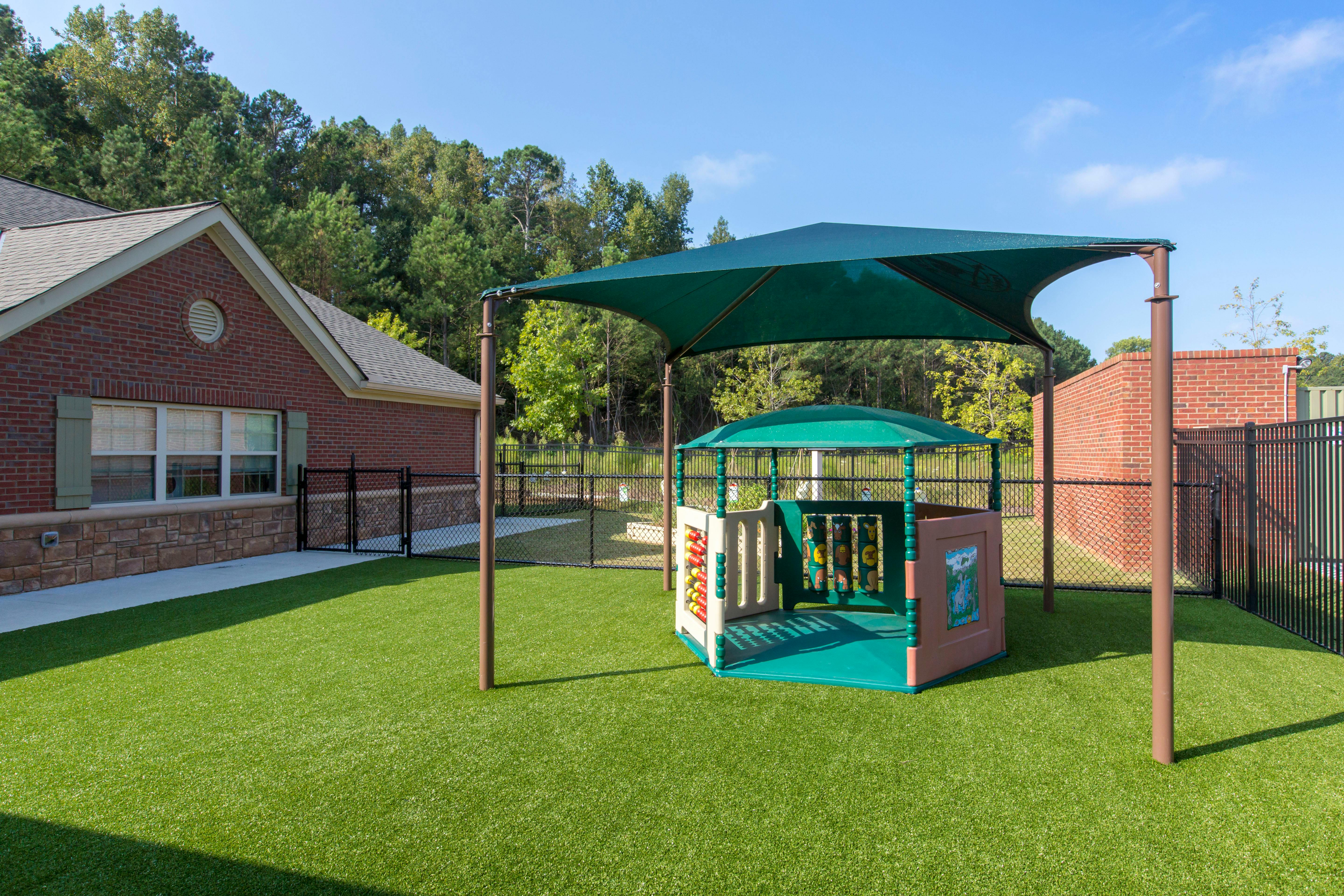 Playground area with artificial turf, a green shade structure, and a play hut