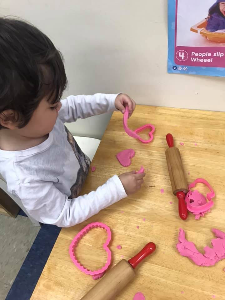 Child playing with pink playdough and heart-shaped cutters
