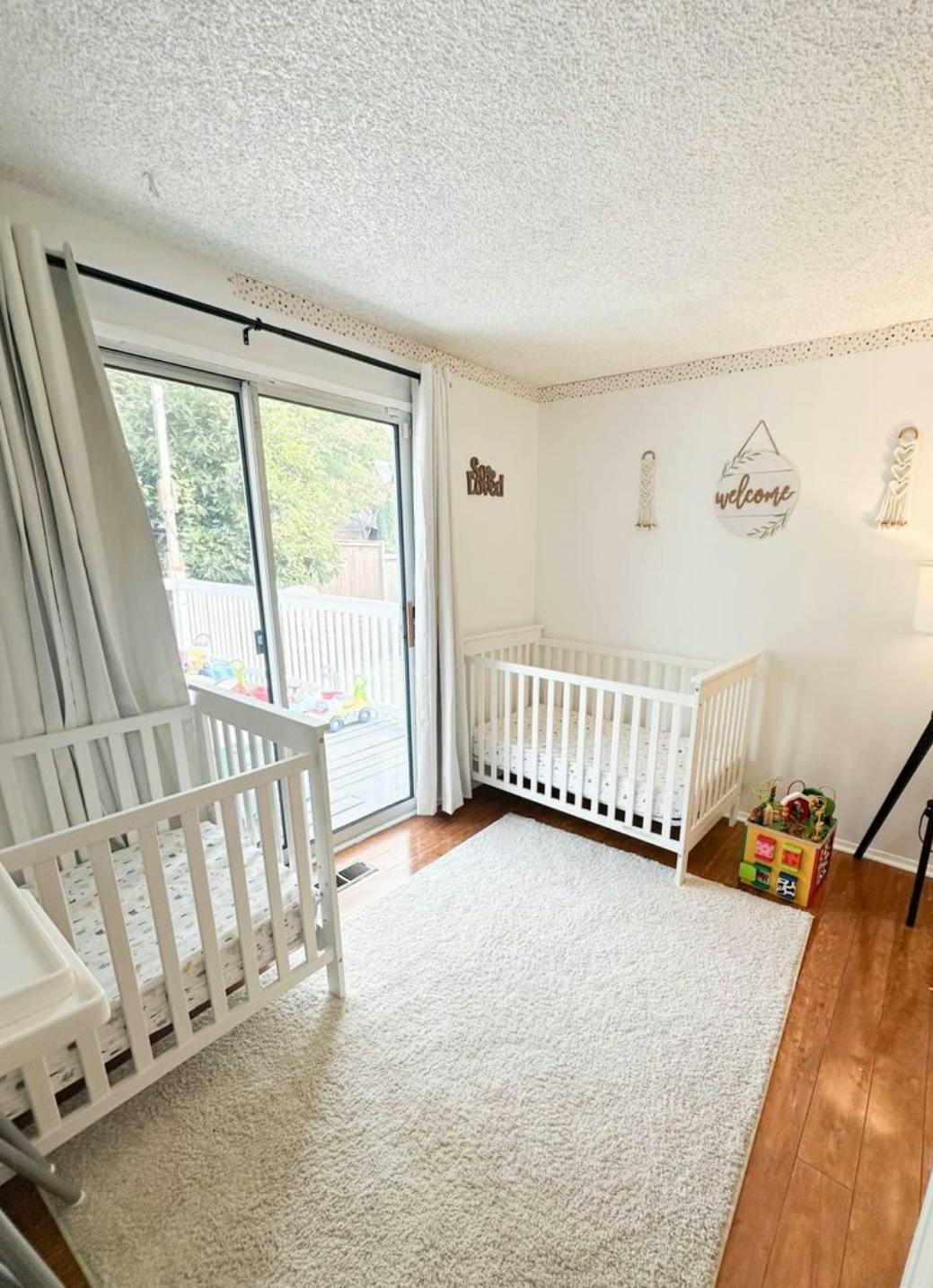 Two white cribs in a room with a sliding glass door