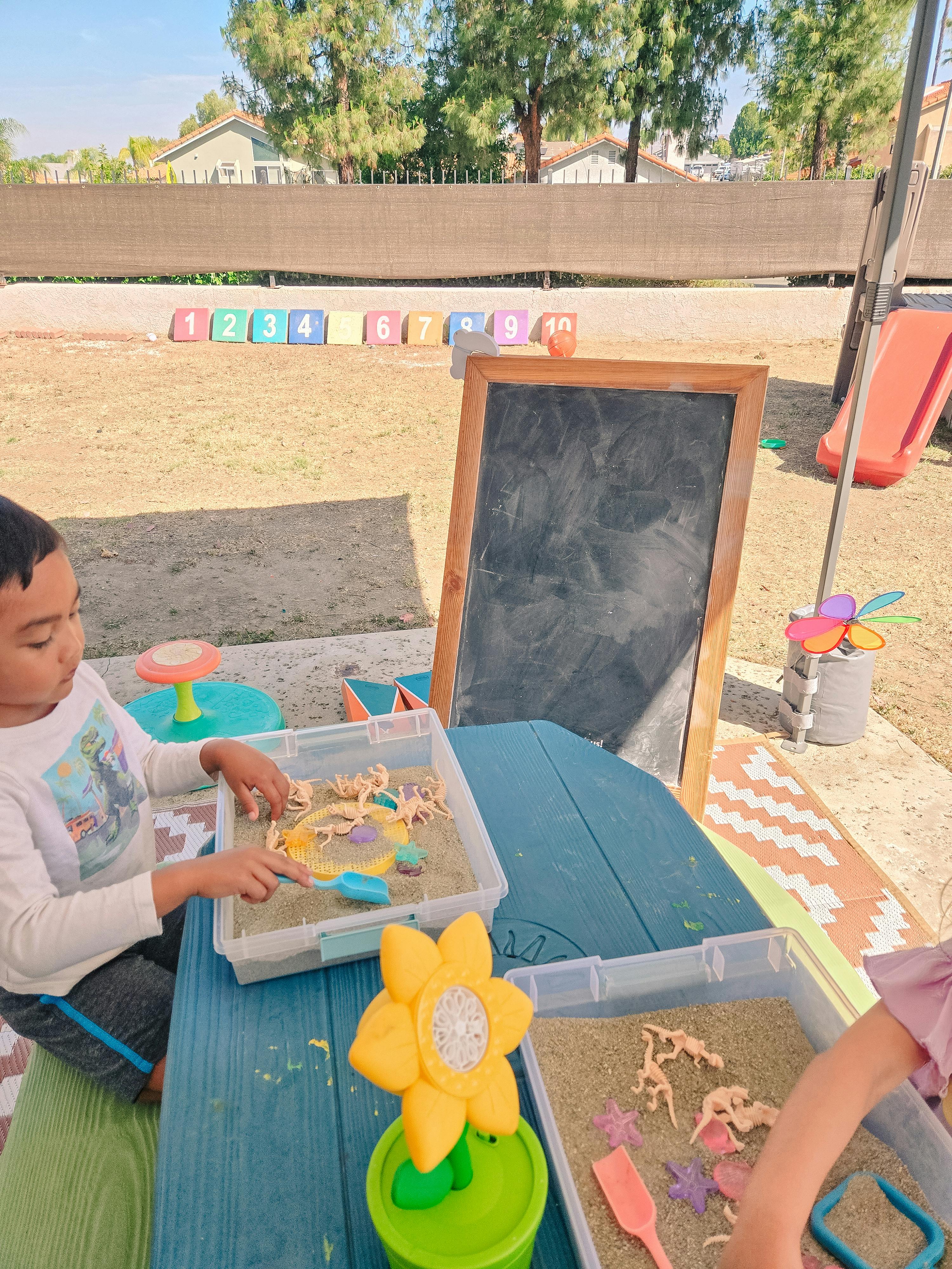 Child playing with sand and toys at an outdoor table