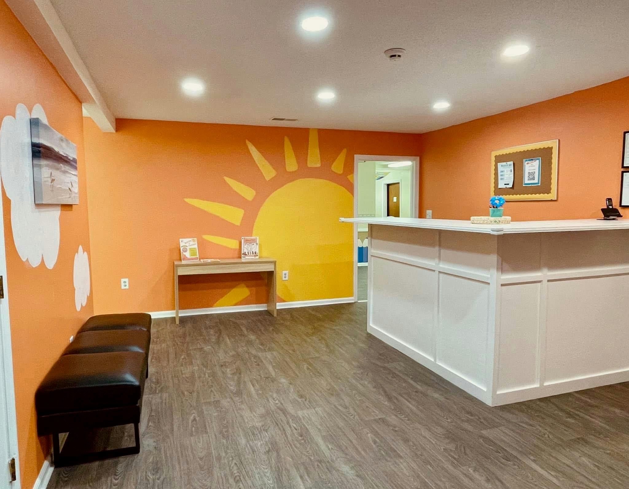 Reception area with a white desk and a large sun mural on an orange wall