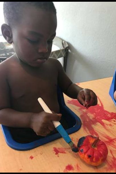 Child painting a small pumpkin with a paintbrush