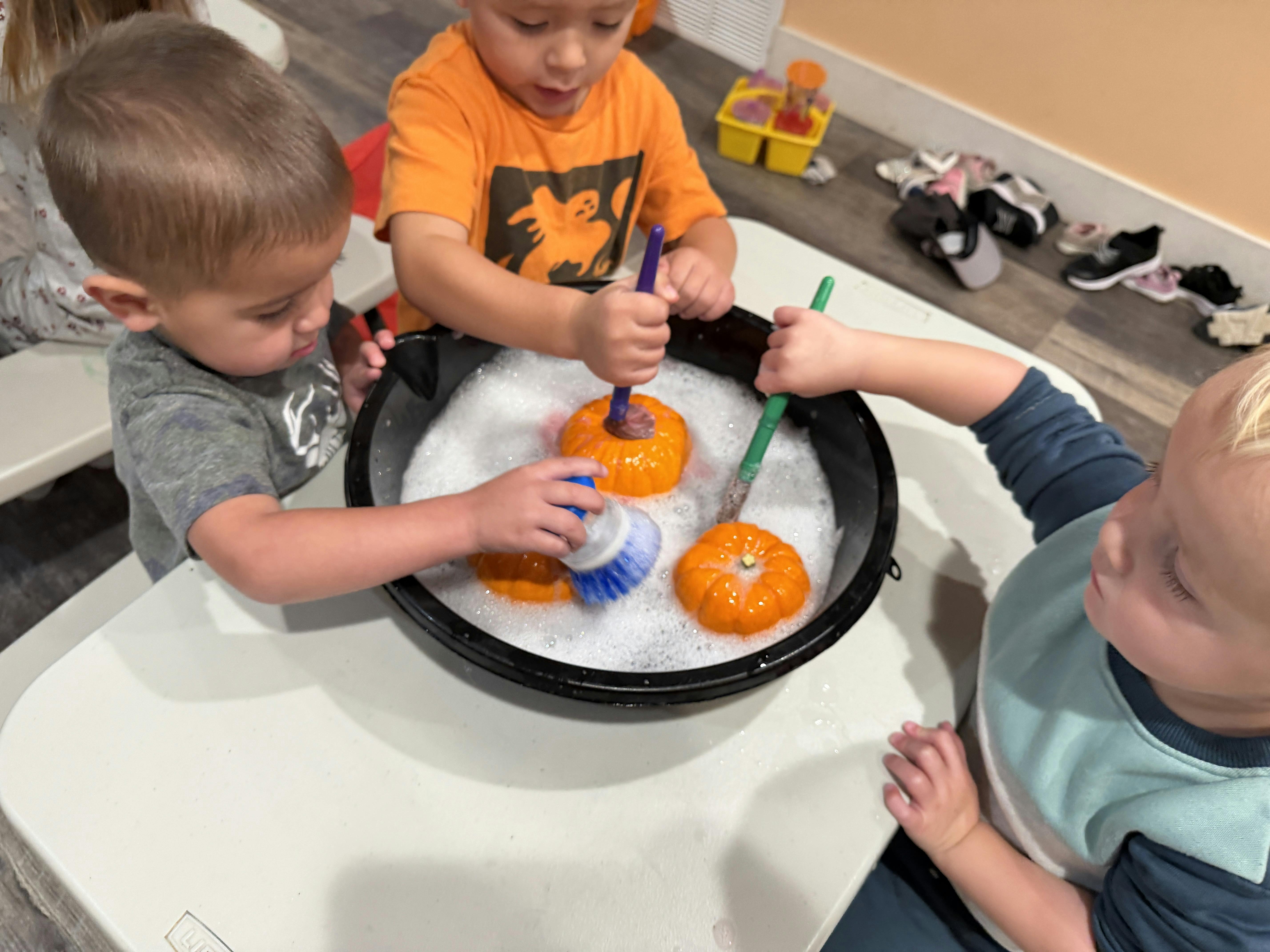 Three children washing small pumpkins in a tub of soapy water