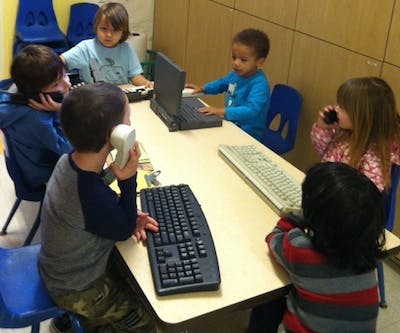 Children at a table with keyboards, laptops, and toy phones