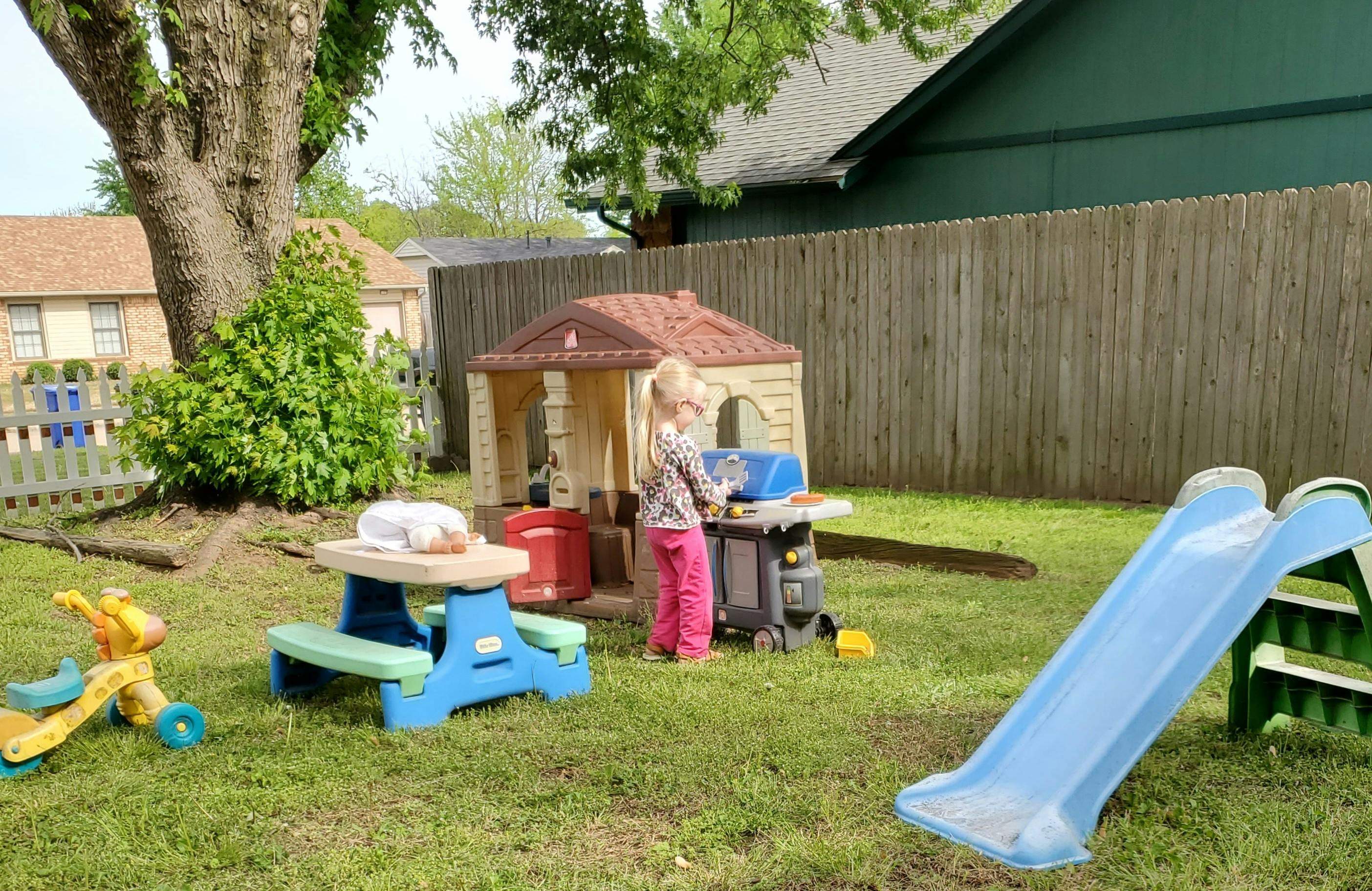 Child playing with a toy grill next to a playhouse in a yard