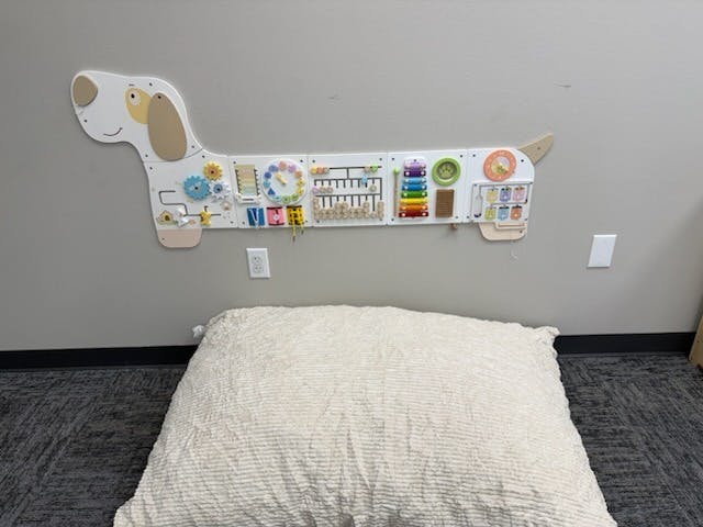 dog-shaped busy board with colorful sensory activities over a large floor cushion