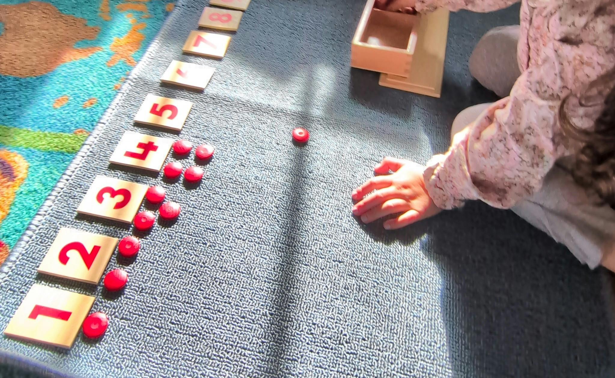 Child learning numbers 1 through 8 with wooden tiles and red counters