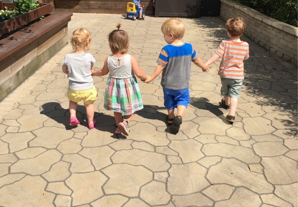 Four children walking away holding hands on a paved path