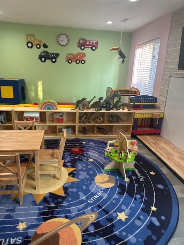 A classroom with a wooden table, shelves with dinosaur toys, and a solar system rug