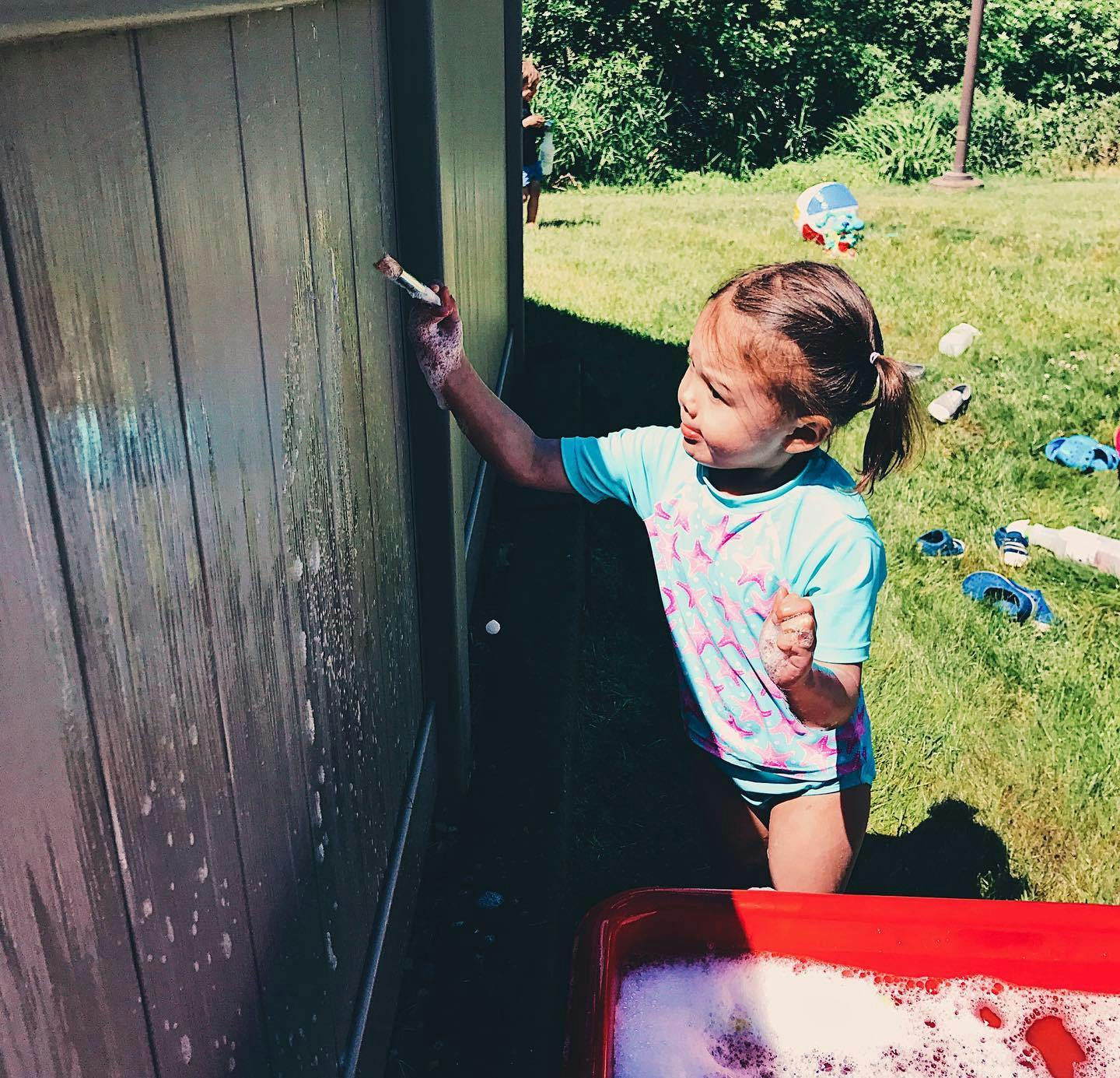 Child painting a wooden fence with a brush