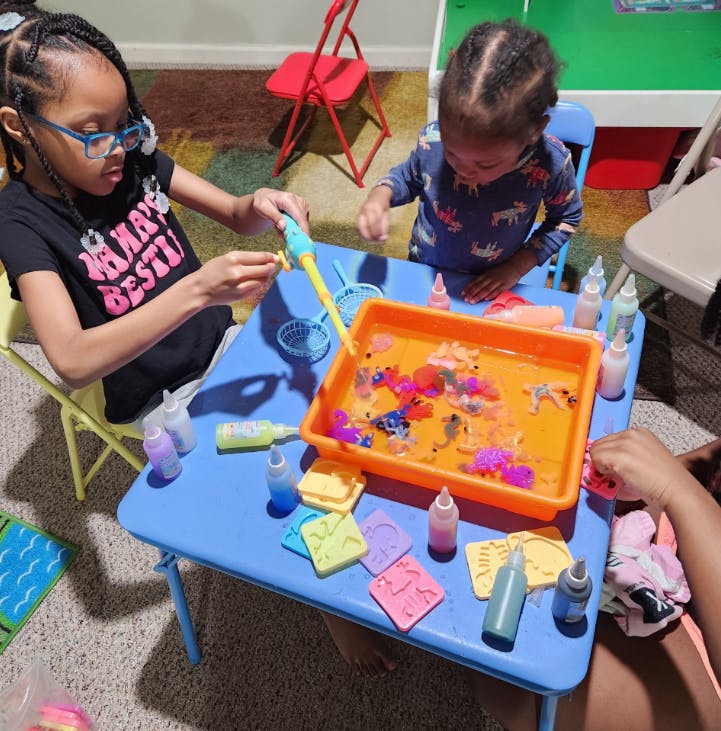Child in glasses playing with a fishing toy next to a tub of water toys