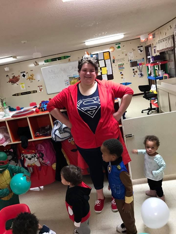 Person in Superman shirt standing with children in a classroom