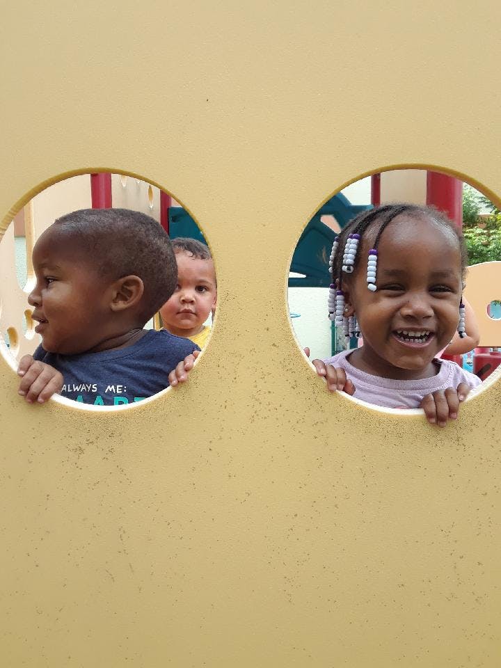 Three children looking through circular openings on a playground