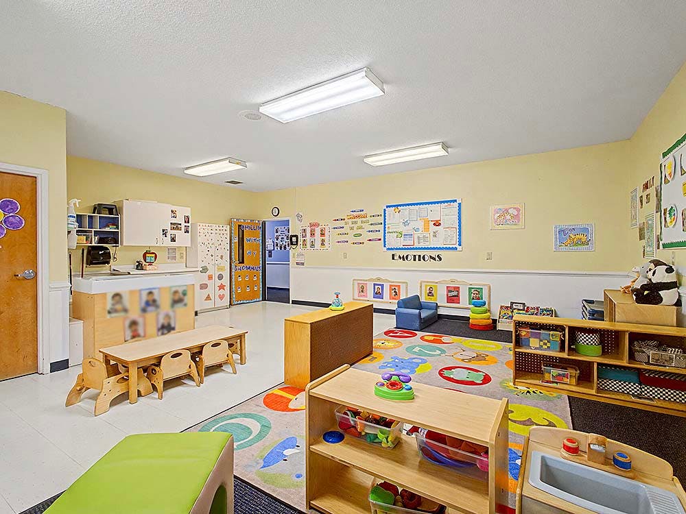 A colorful empty classroom with small tables, chairs, and play areas