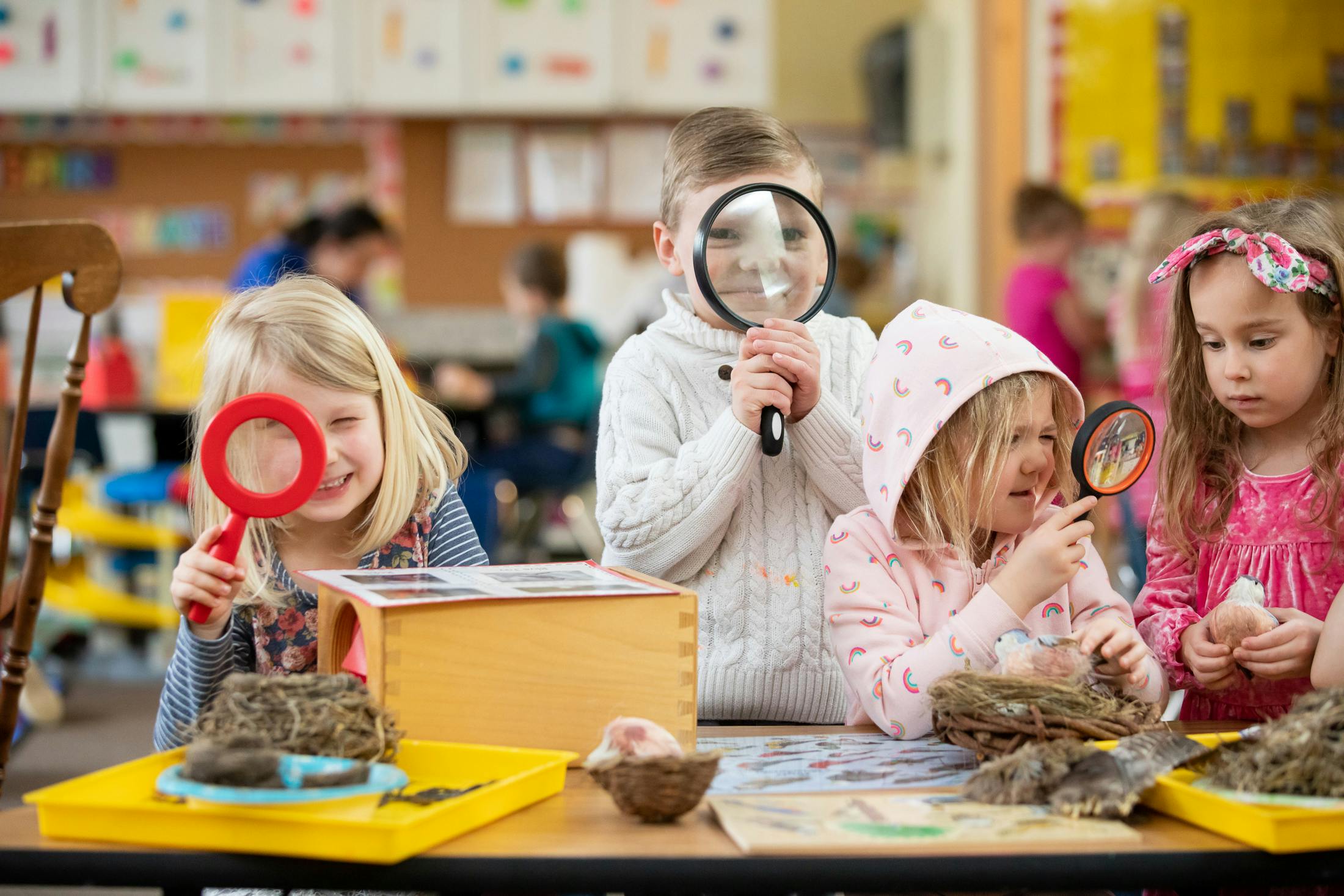 Children looking through magnifying glasses at objects in a classroom