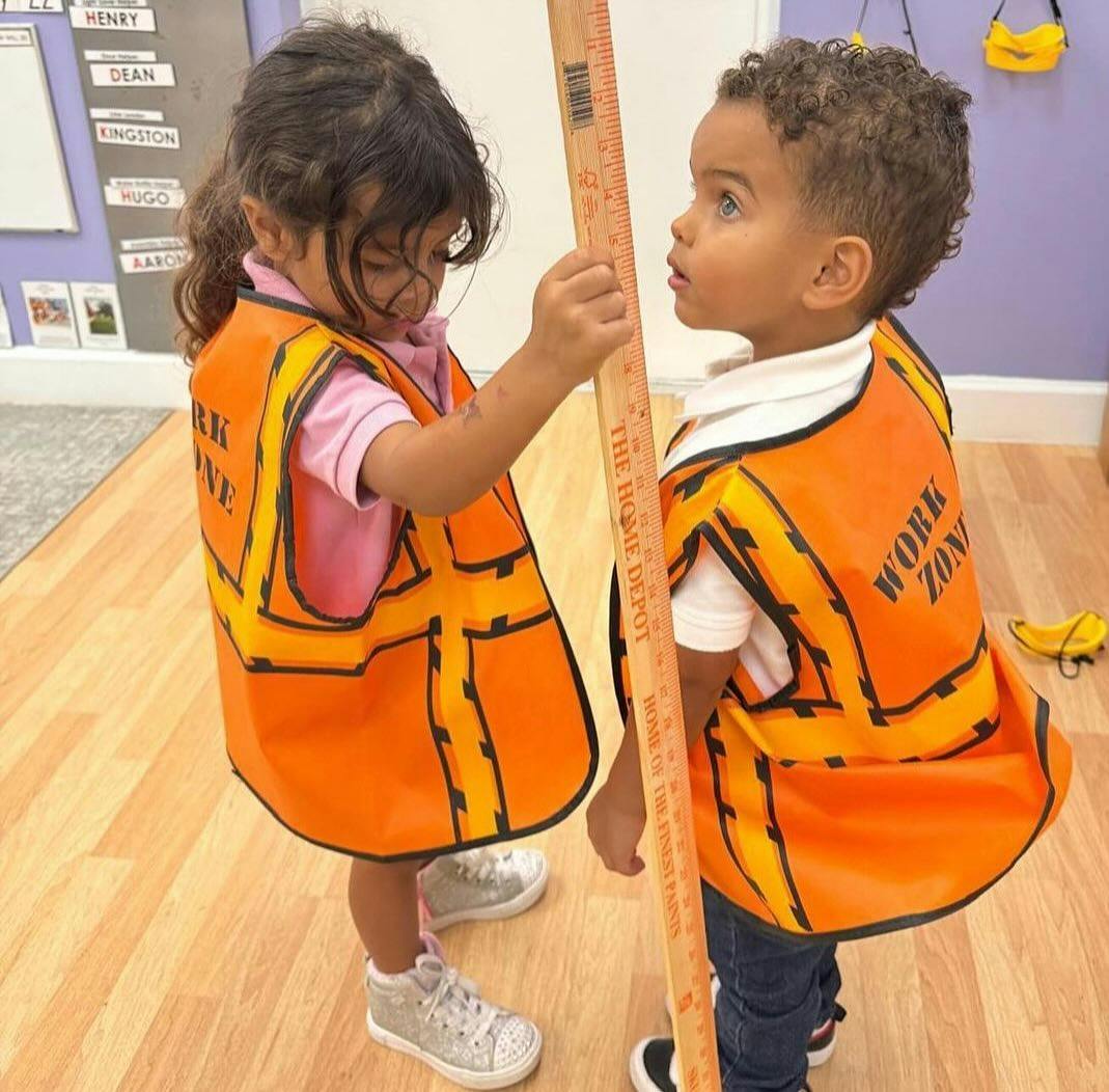 Two children in orange vests holding a long ruler