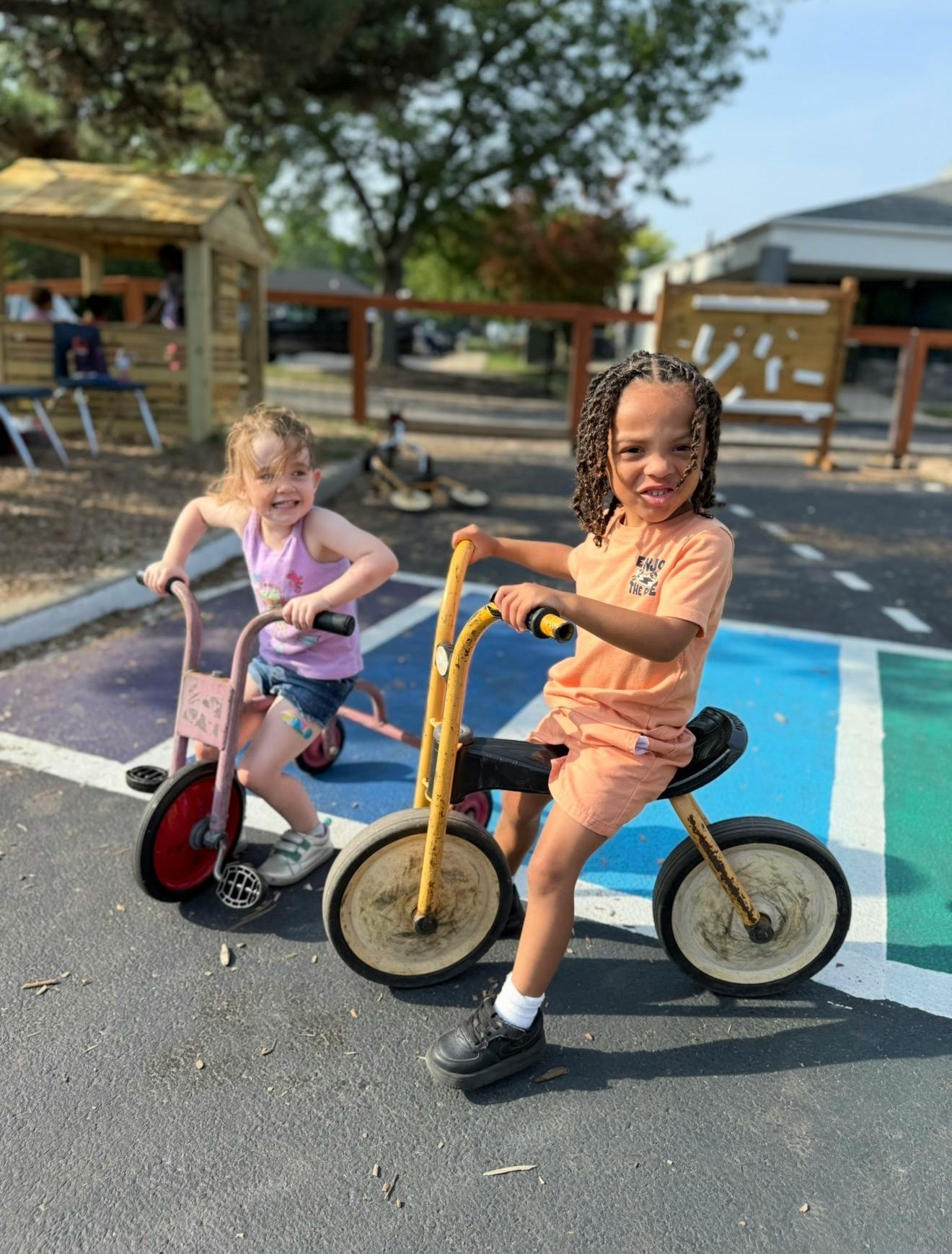 Two children riding small tricycles on an outdoor play area