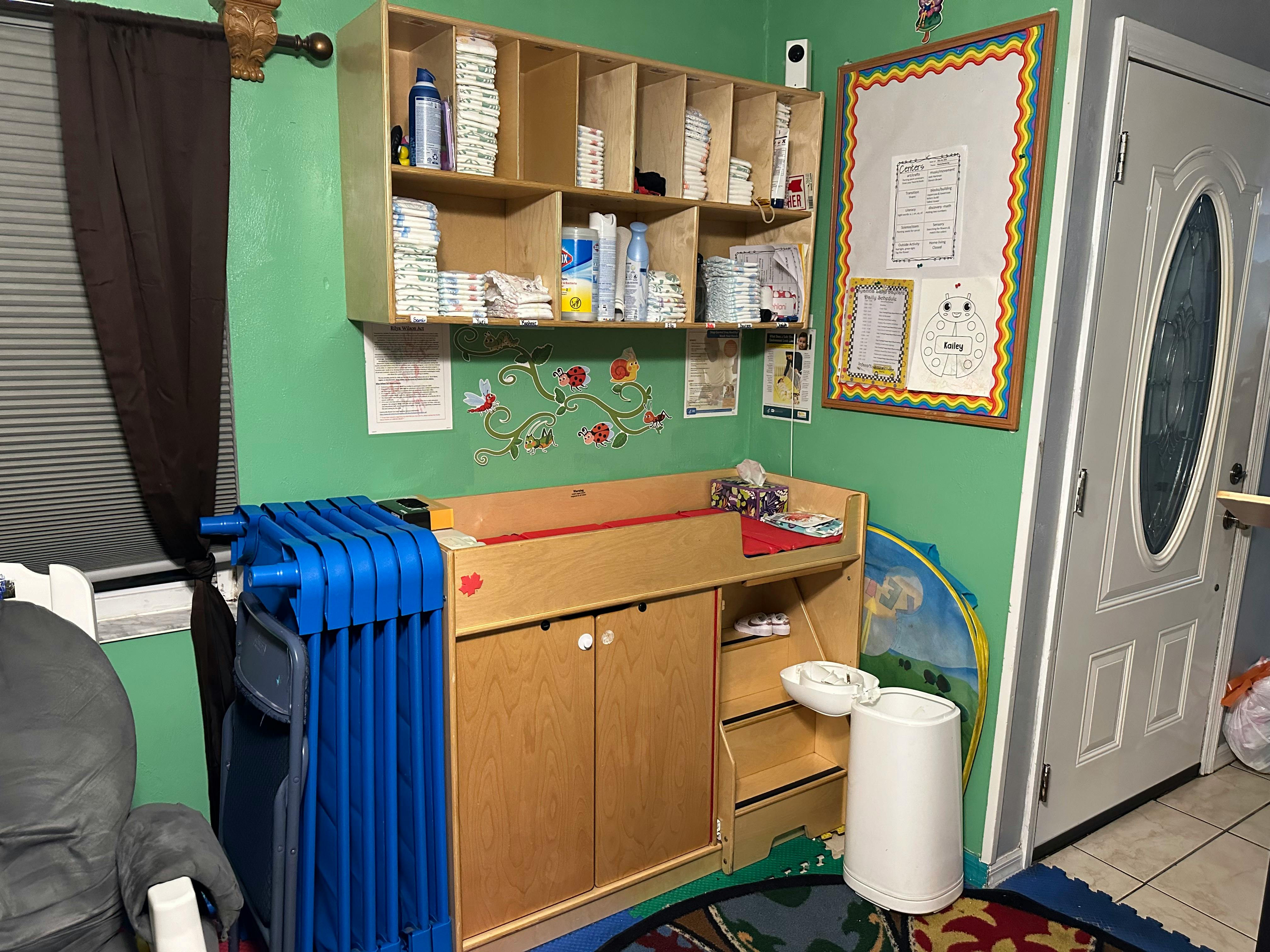 Changing station with shelves of supplies and a blue cot in-home playpen