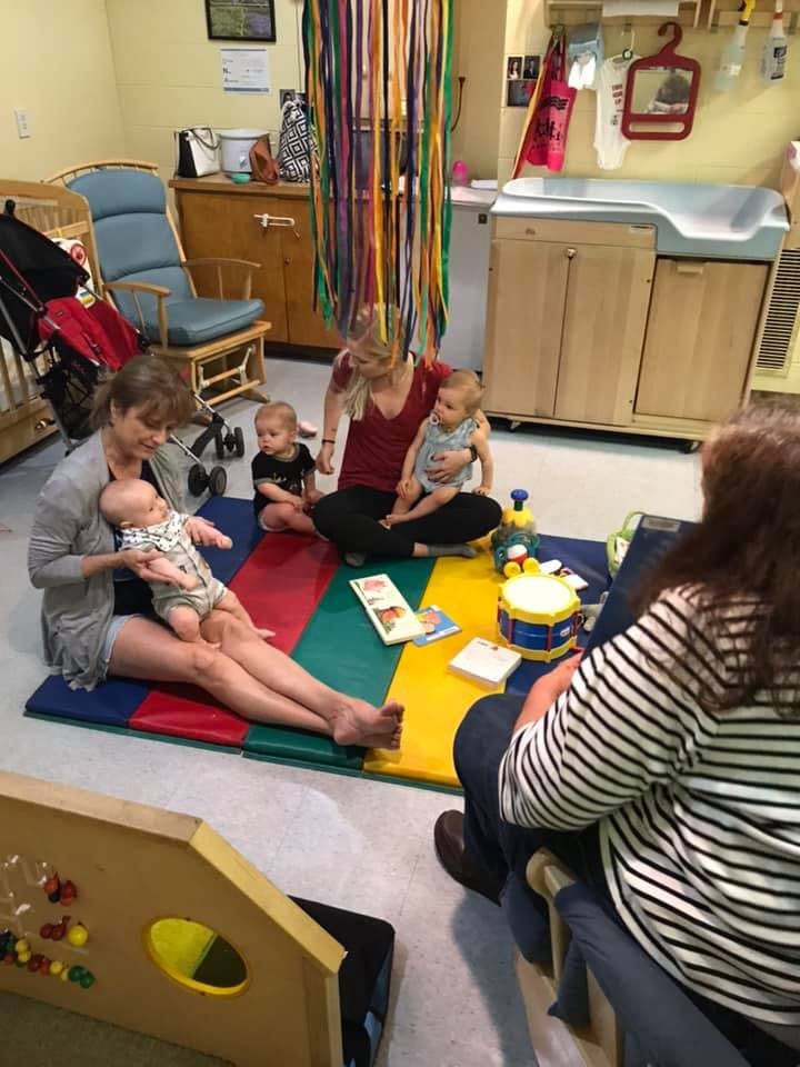 Adults and children sitting on a colorful mat in a room