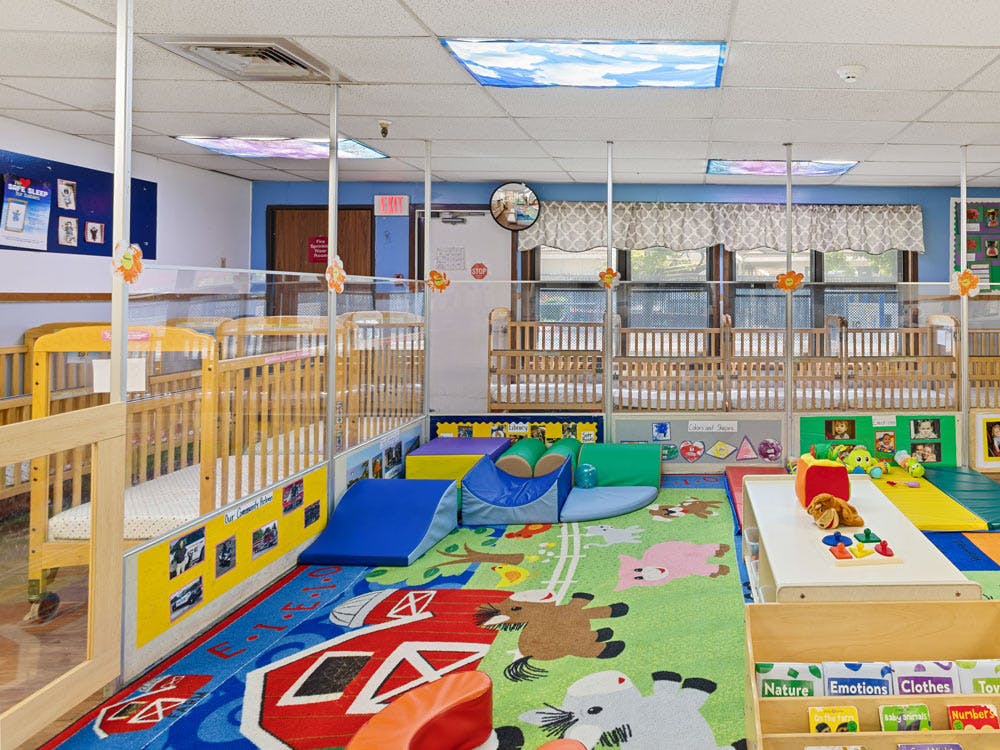 Cribs separated by clear partitions in an infant classroom with playmats and toys