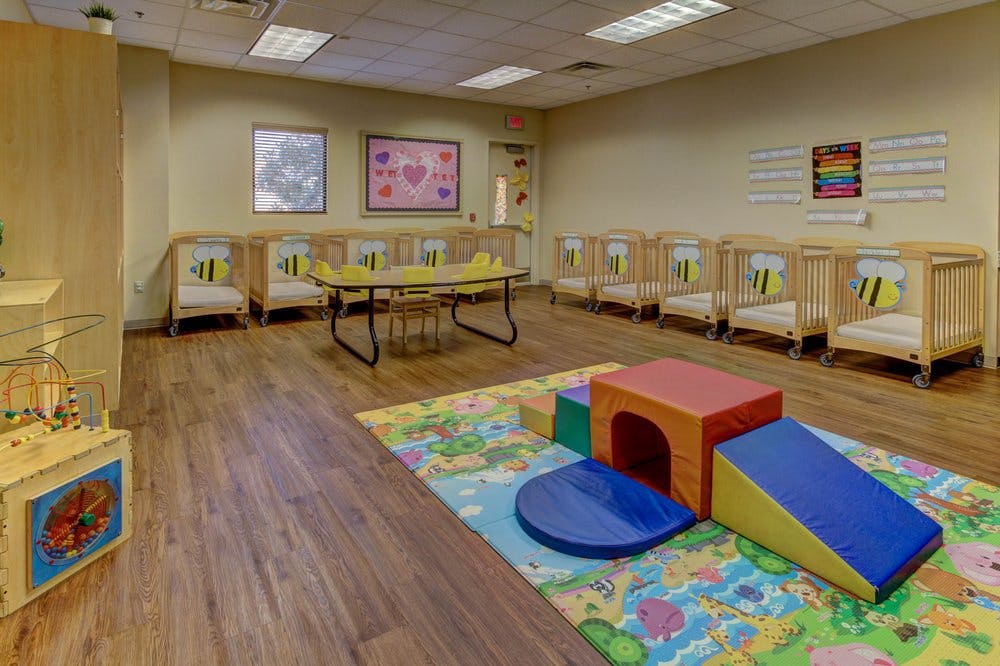Playroom with soft play equipment on a colorful rug and cribs along the wall