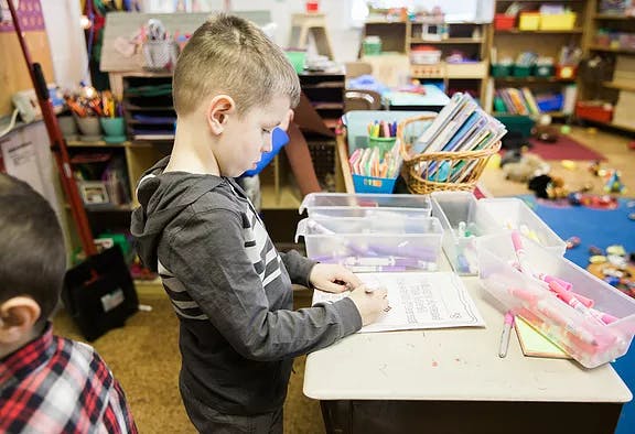Child writing at a table in a classroom