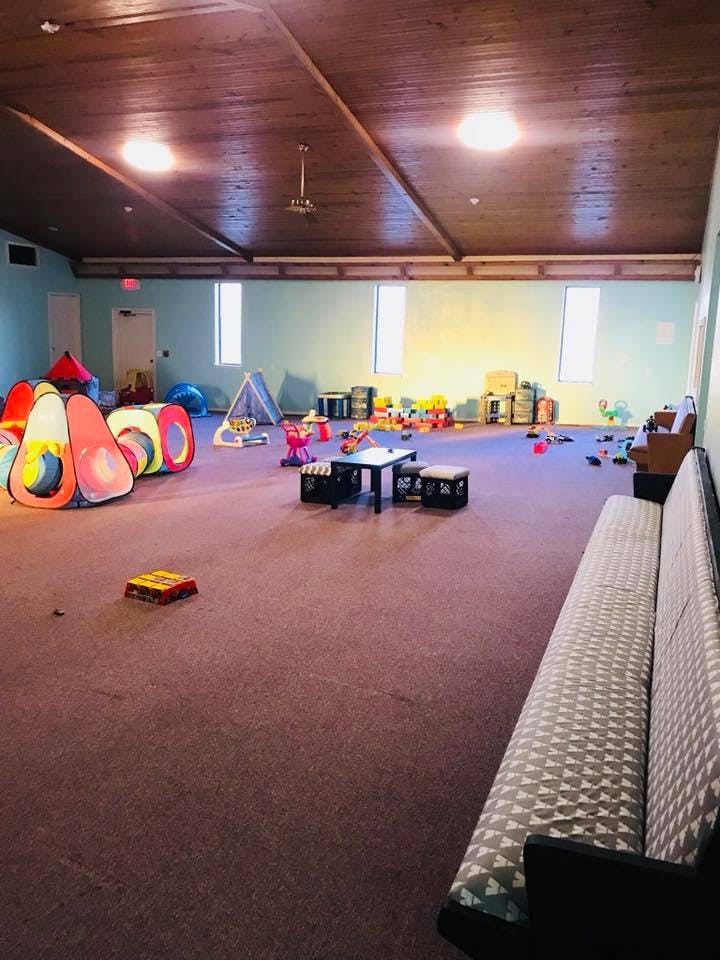 Playroom with colorful play tunnels, small tables, and toys on the right a long bench
