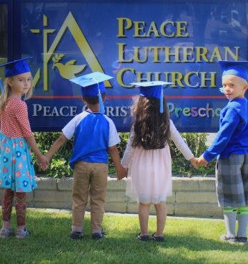 Four children in graduation caps holding hands in front of a banner