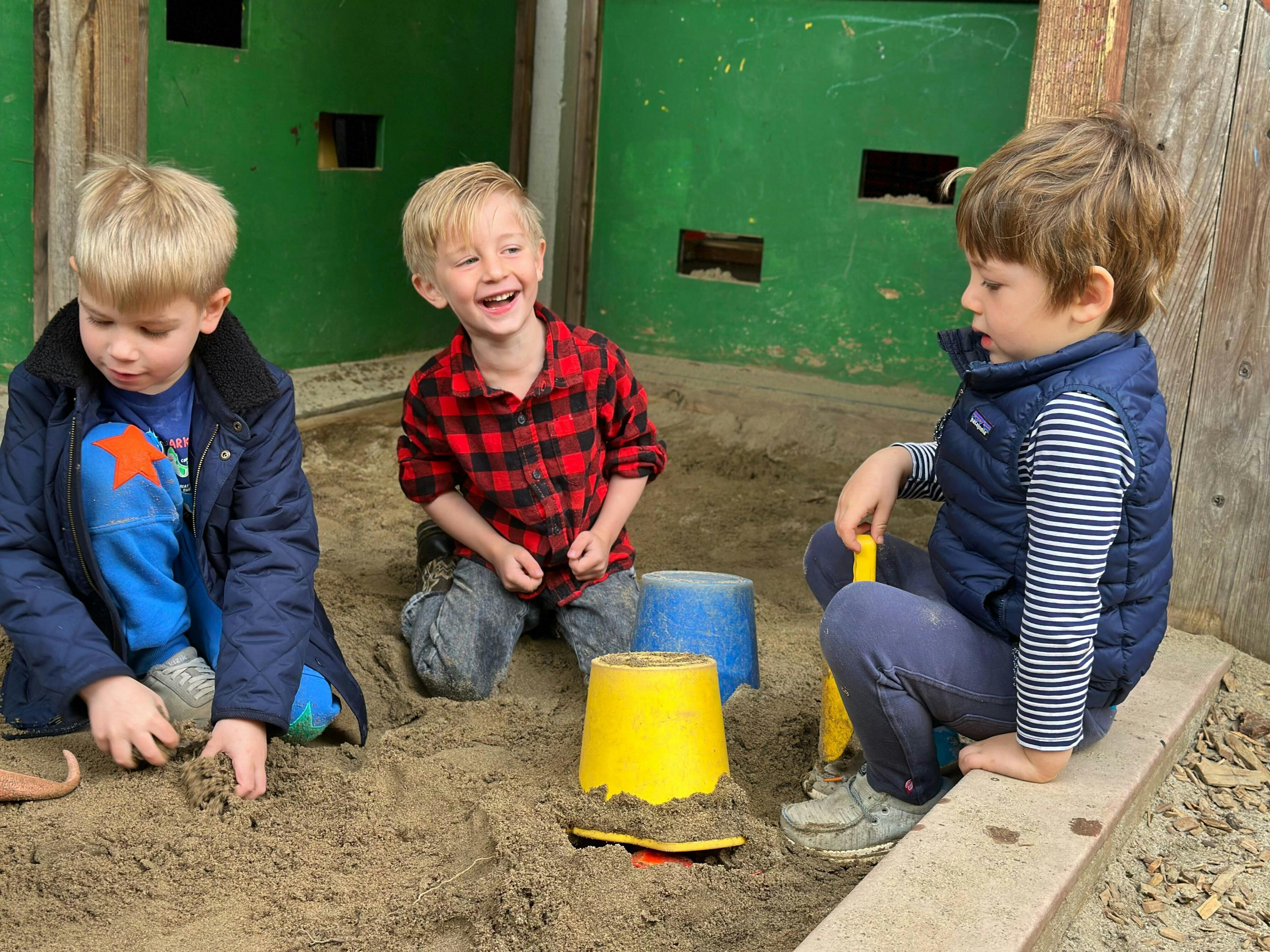 Three children playing in a sandbox with buckets