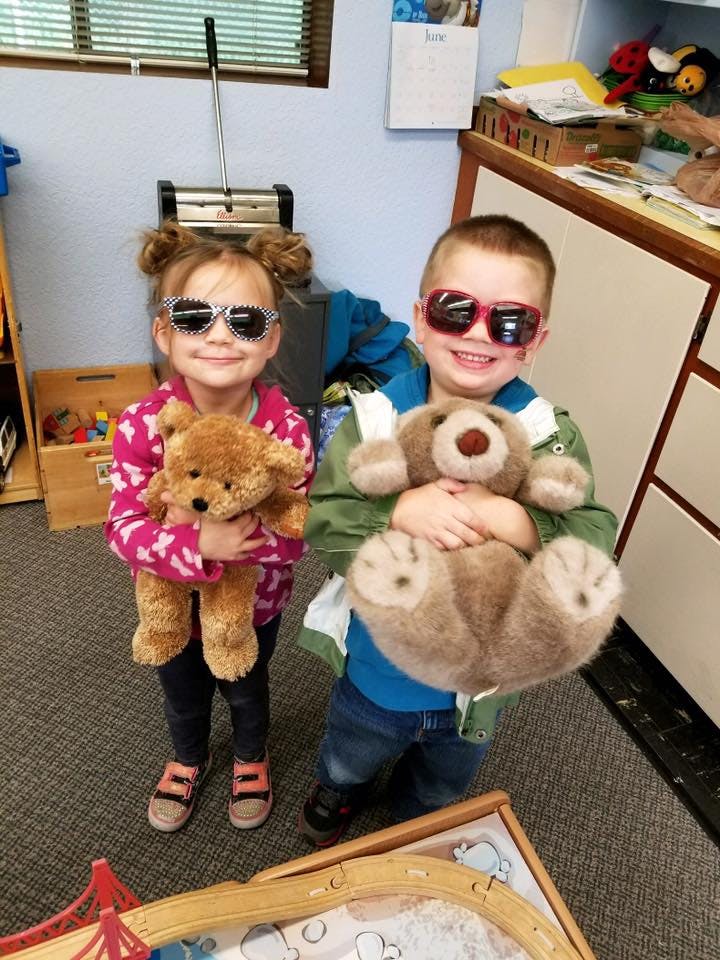 Two children wearing sunglasses and holding teddy bears