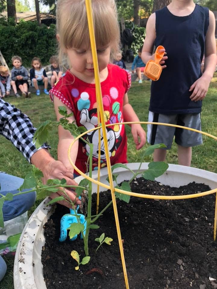Adult and child planting in a large pot with other children in the background