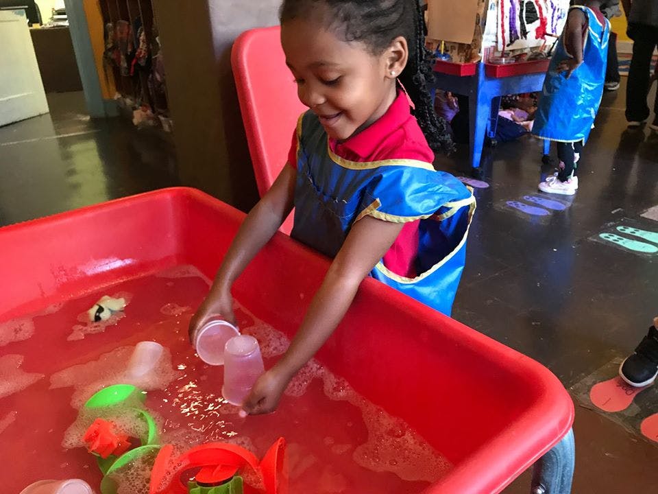 Child playing with water and cups in a red water table
