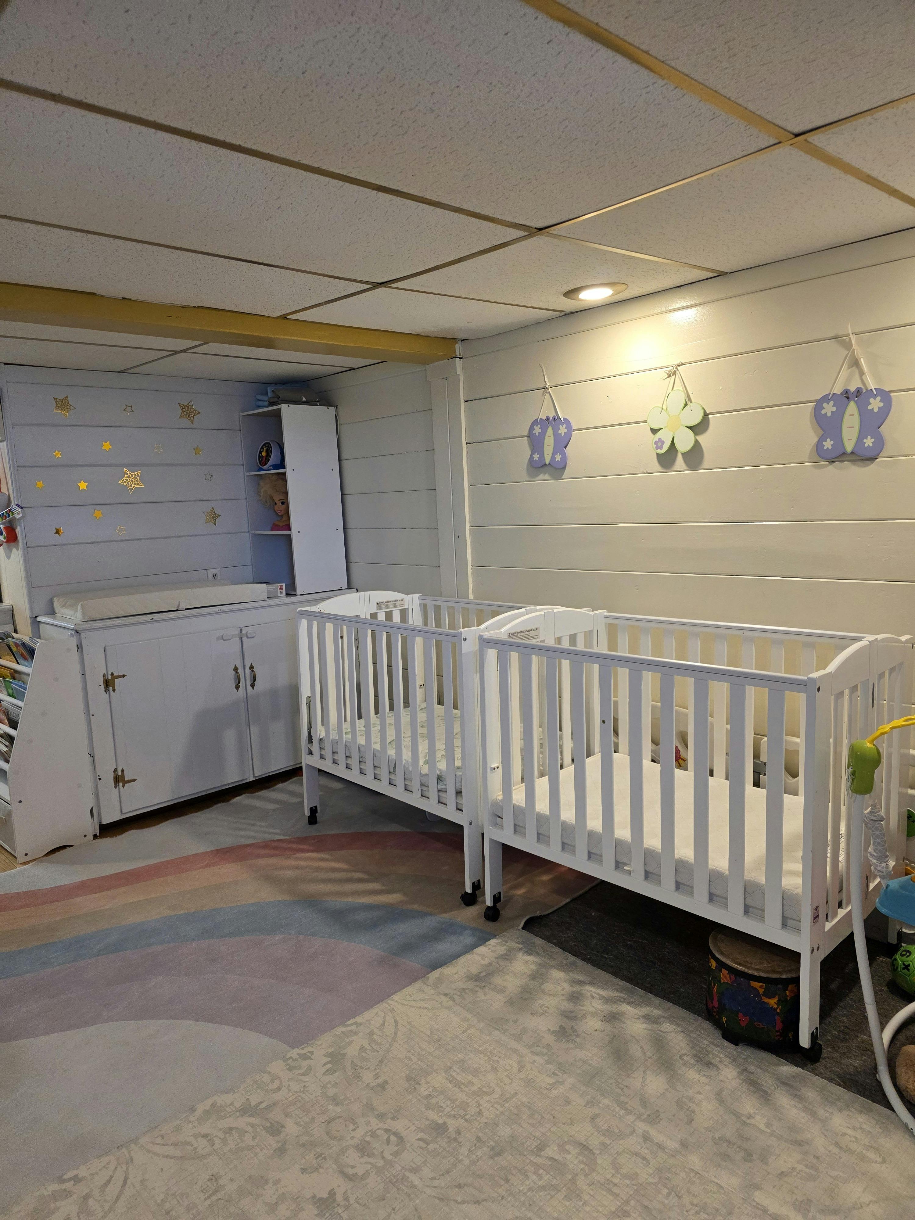 Two white cribs and a changing table in a nursery