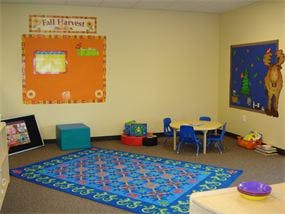 Empty classroom with small tables and chairs, a rug, and wall decorations