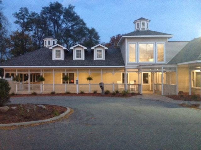 Building with cupolas, dormers, and a large porch, with a paved area in front