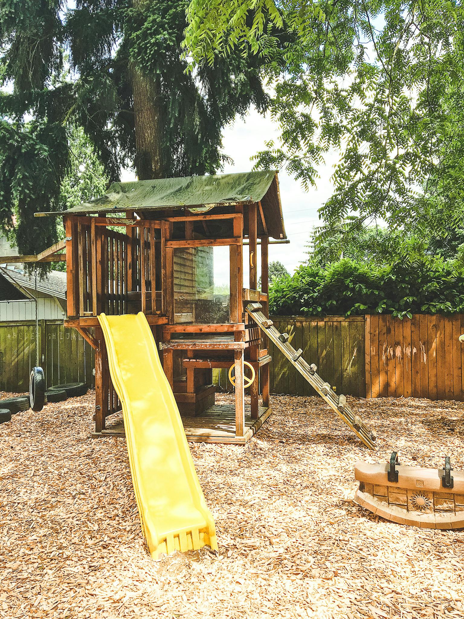 Wooden playhouse with a yellow slide and ladder on a wood chip ground