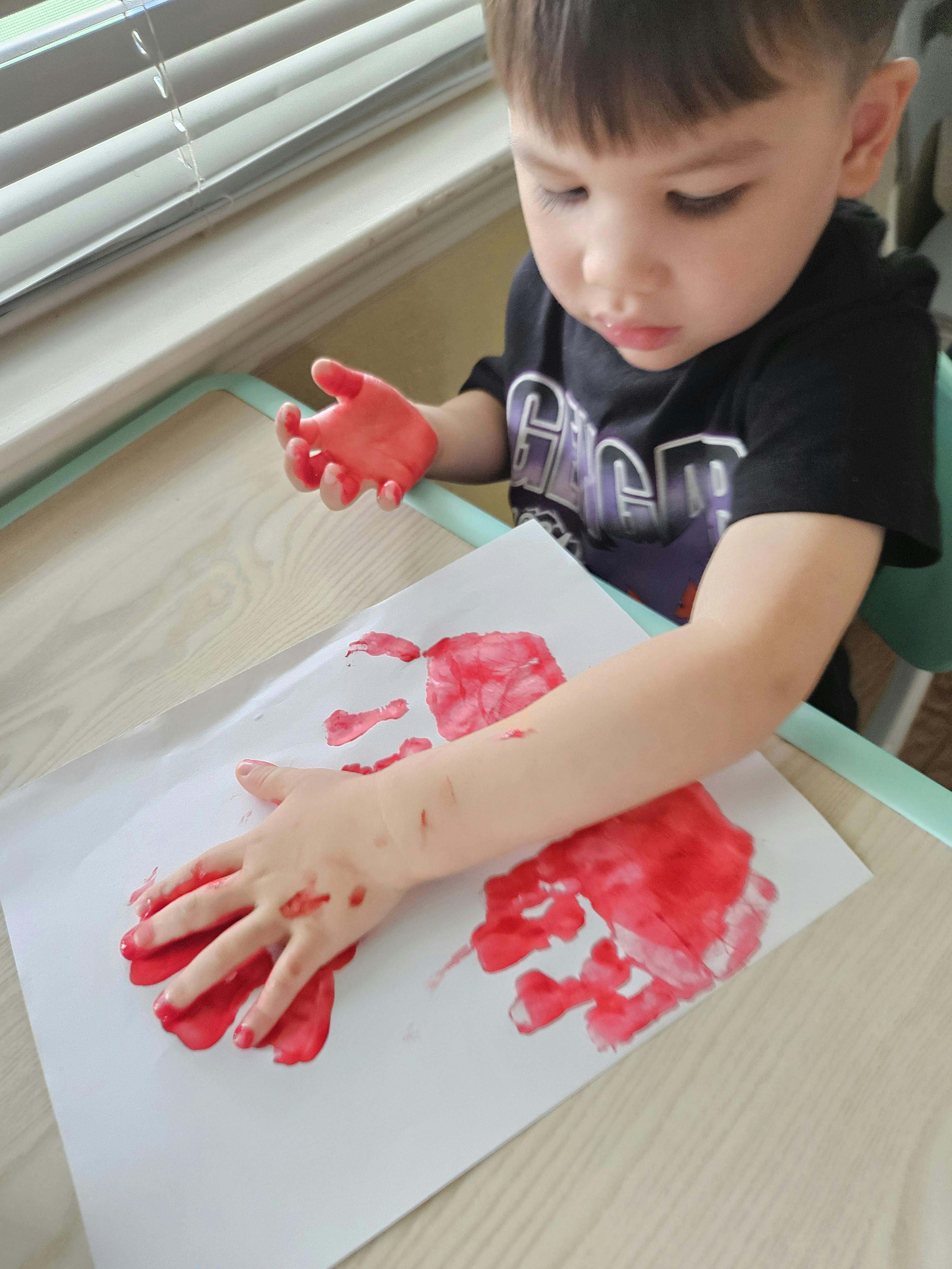 Child making a red handprint on white paper