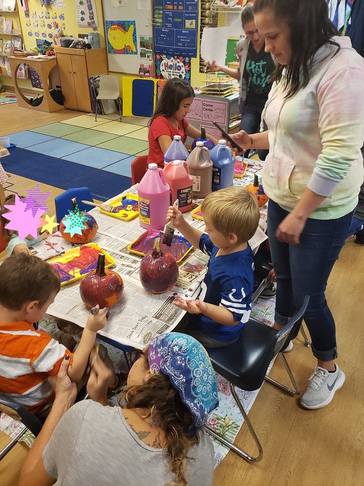 Adults and children painting pumpkins at a table