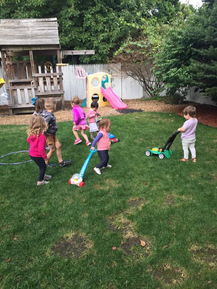 Children playing with toy lawnmowers in a grassy backyard