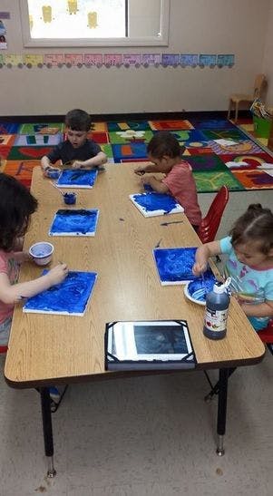 Children painting at a table in a classroom